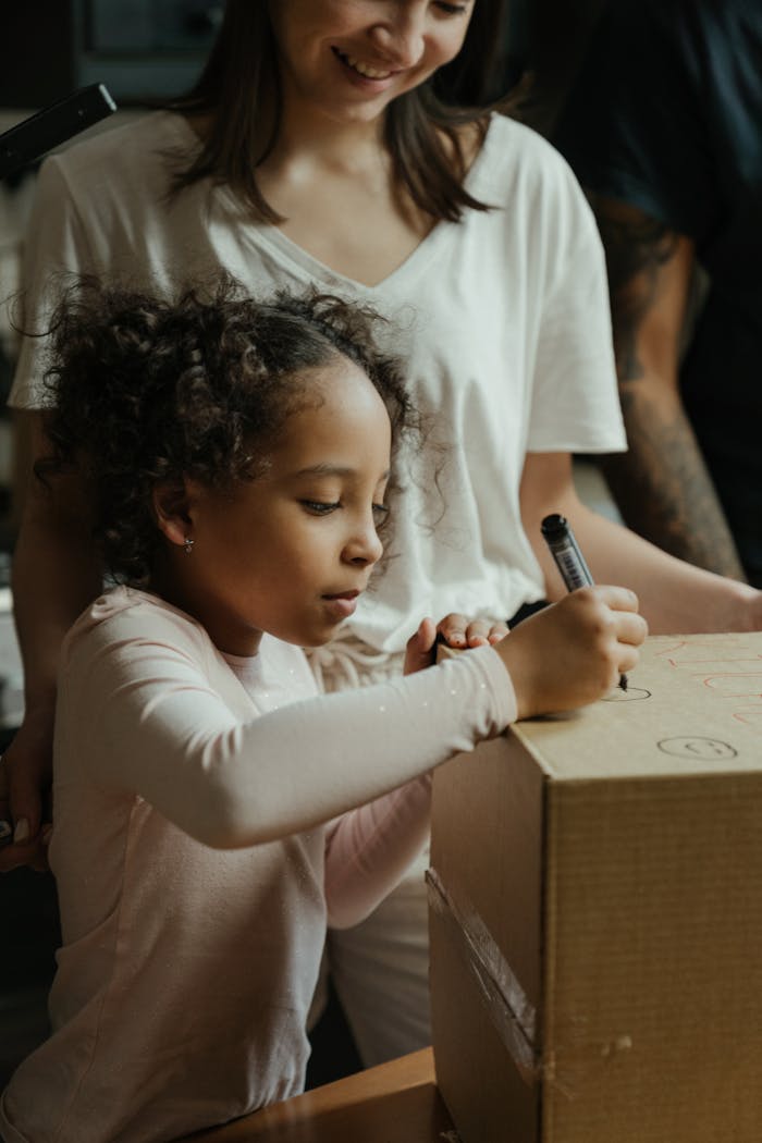 A mother and daughter enjoy a moment together writing on a moving box in their new home.